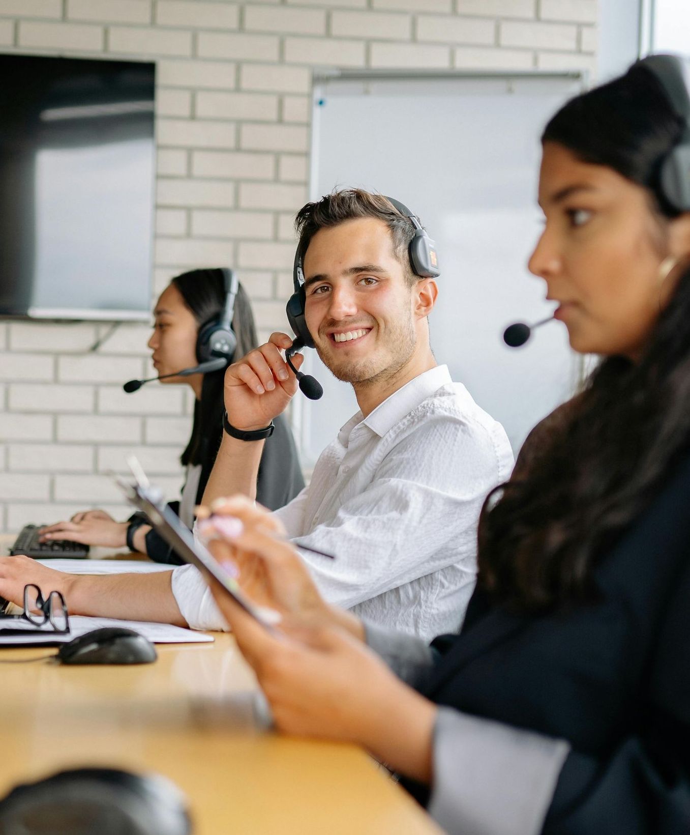 A man wearing a headset is sitting at a desk with other people.