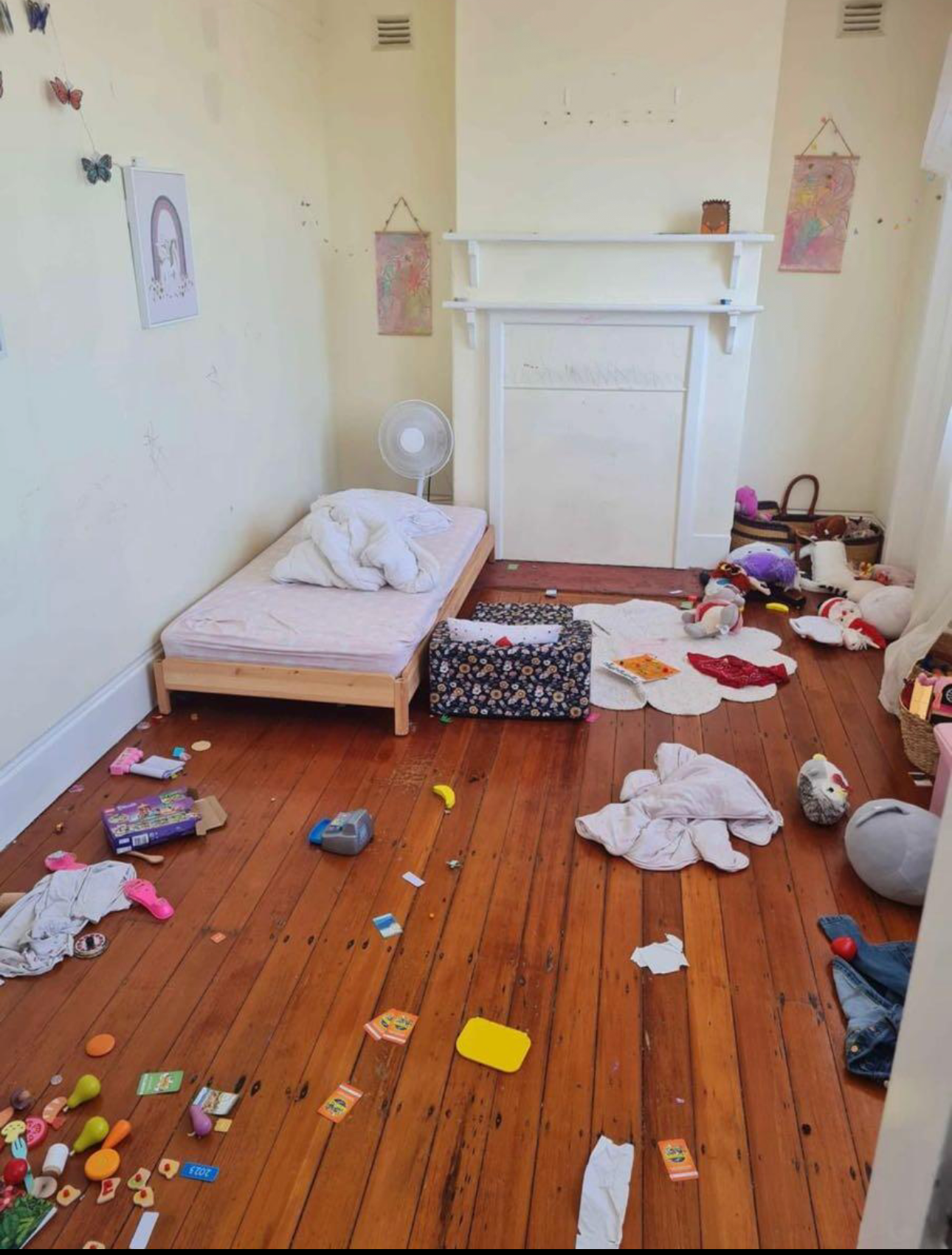 Messy child's bedroom with toys scattered on the wood floor. A bed, dresser, and fireplace are visible.