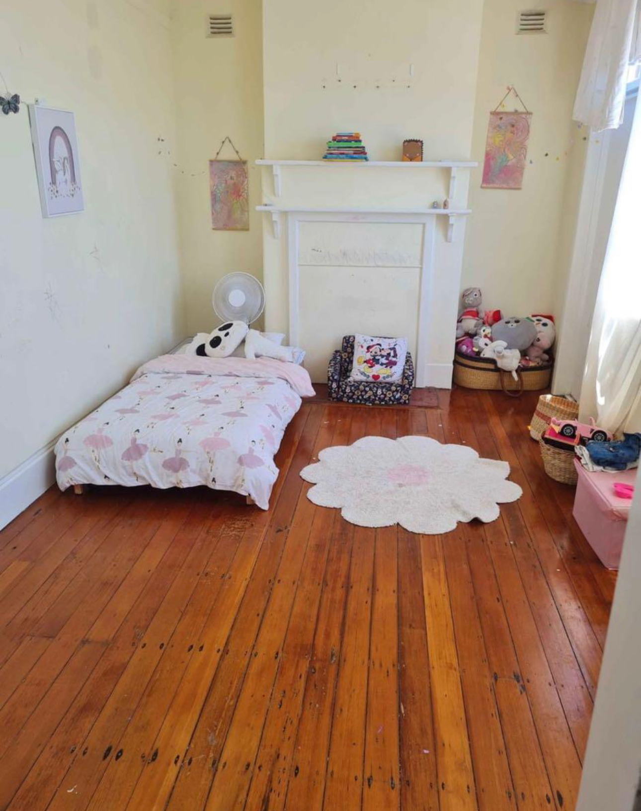 Bedroom with hardwood floors, a bed, fireplace, and toys. Light pink and white decor.