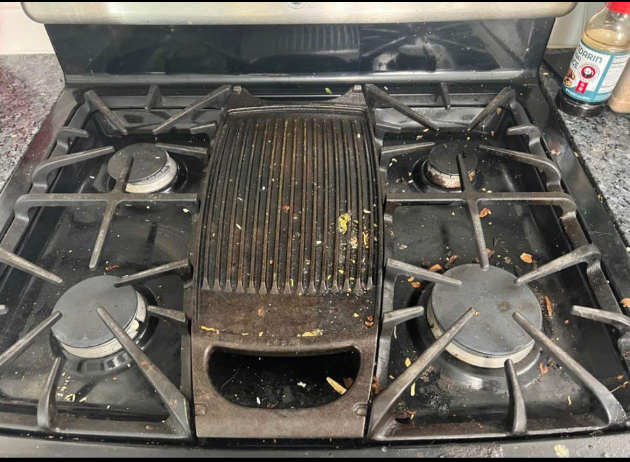 Dirty stovetop with a grill in the center and burner grates, covered in food debris.