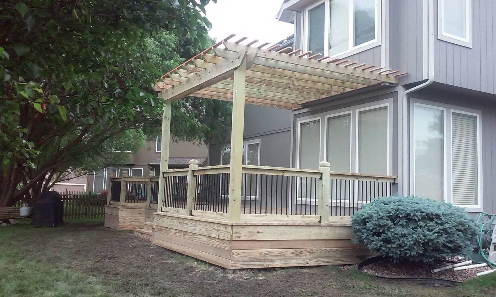 A wooden deck with a pergola is in front of a house.