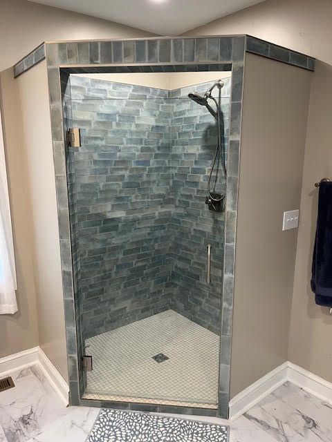 Corner shower with blue tiled walls, glass door, and white tiled floor.
