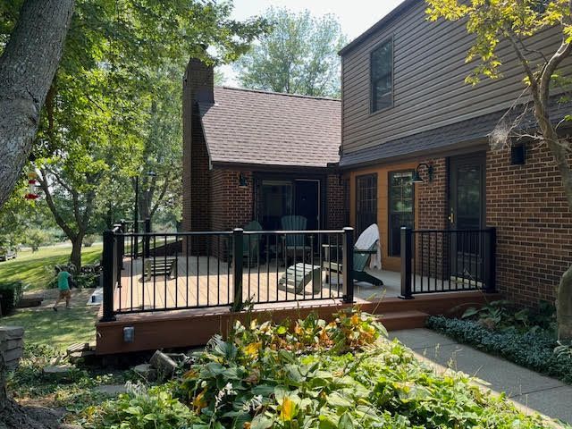 Wooden deck with black railing attached to a two-story brick house, with trees and a grassy yard.