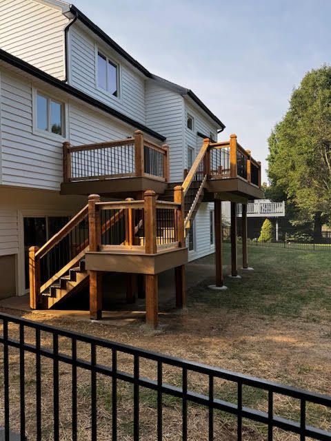 Multi-level wooden deck with stairs attached to a two-story white house, surrounded by a grassy yard.