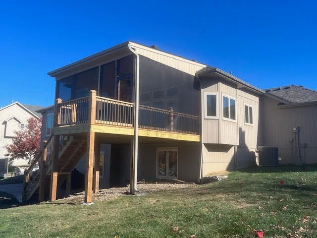 Screened-in deck attached to a beige house, with stairs leading down to the backyard. Clear blue sky.