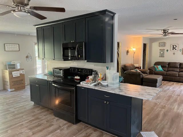 Navy blue kitchen cabinets with appliances and a light wood-look floor; a living room is visible in the background.