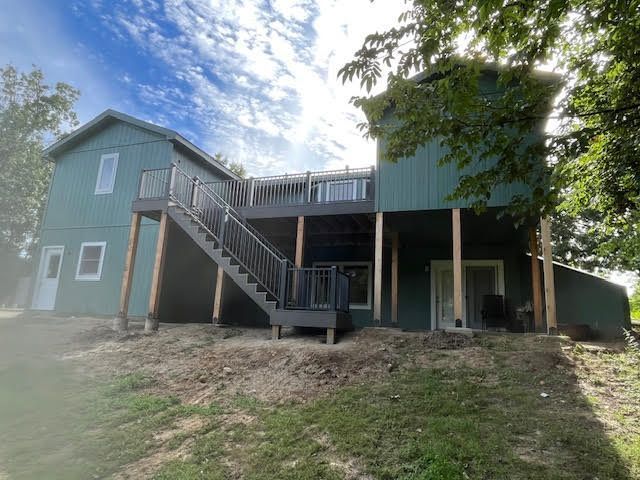 Green house with gray decks and stairs on a grassy hill under a partly cloudy sky.