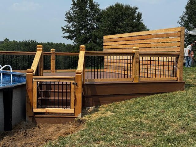 A wooden deck with a staircase leading to an above-ground pool. Brown and black railings surround the deck.