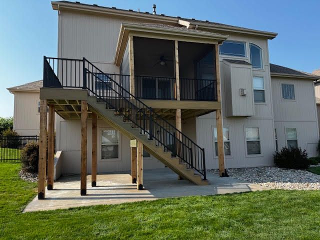 Backyard deck with stairs to a screened-in porch, beige house, black railing, tan deck, on concrete.