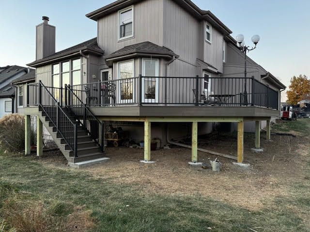 Back of a two-story beige house with a new deck; black railings and stairs; a grassy yard.