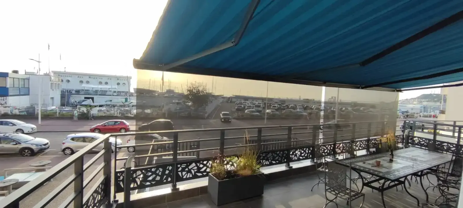 Un balcon avec tables et chaises sous un auvent bleu.
