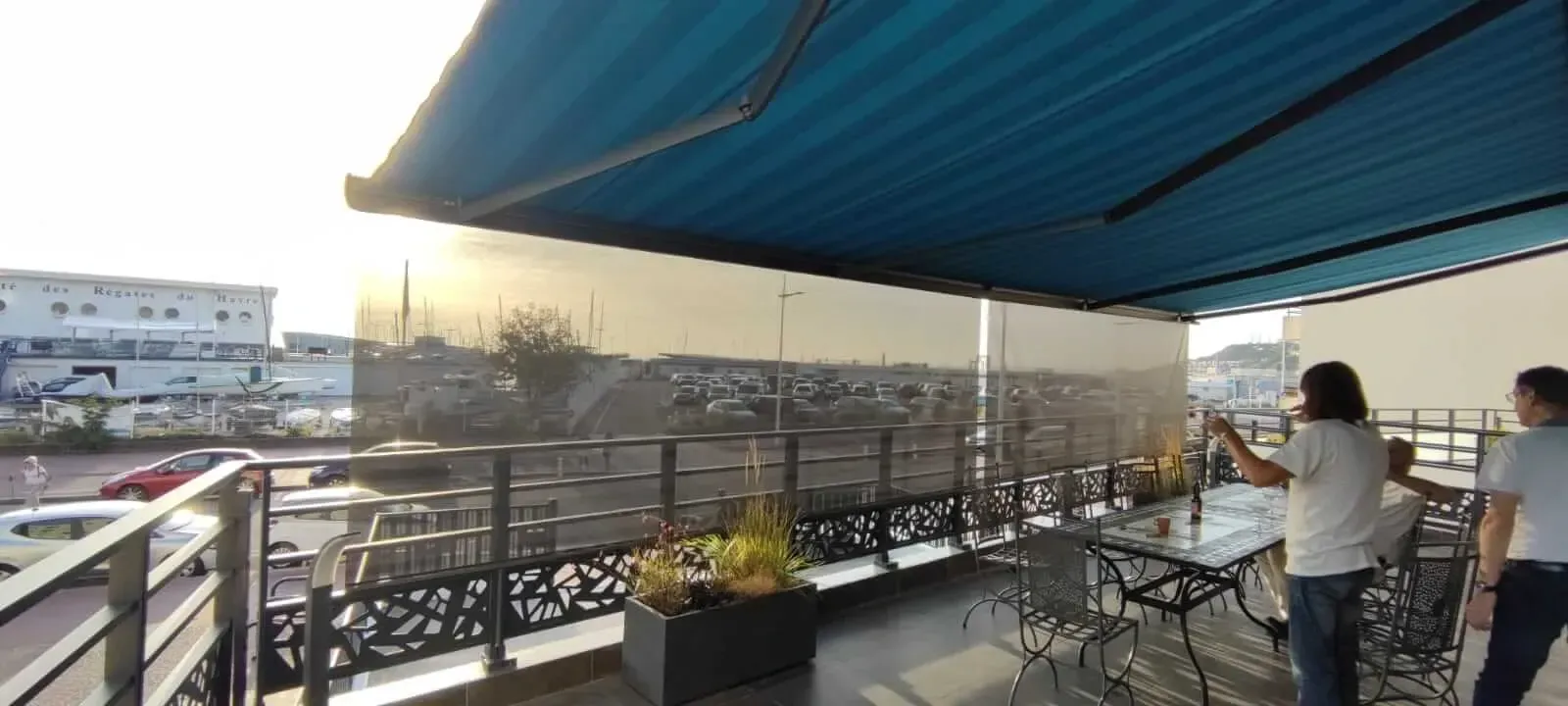 Deux personnes se tiennent sous store extérieur sur un balcon avec vue sur la plage du Havre