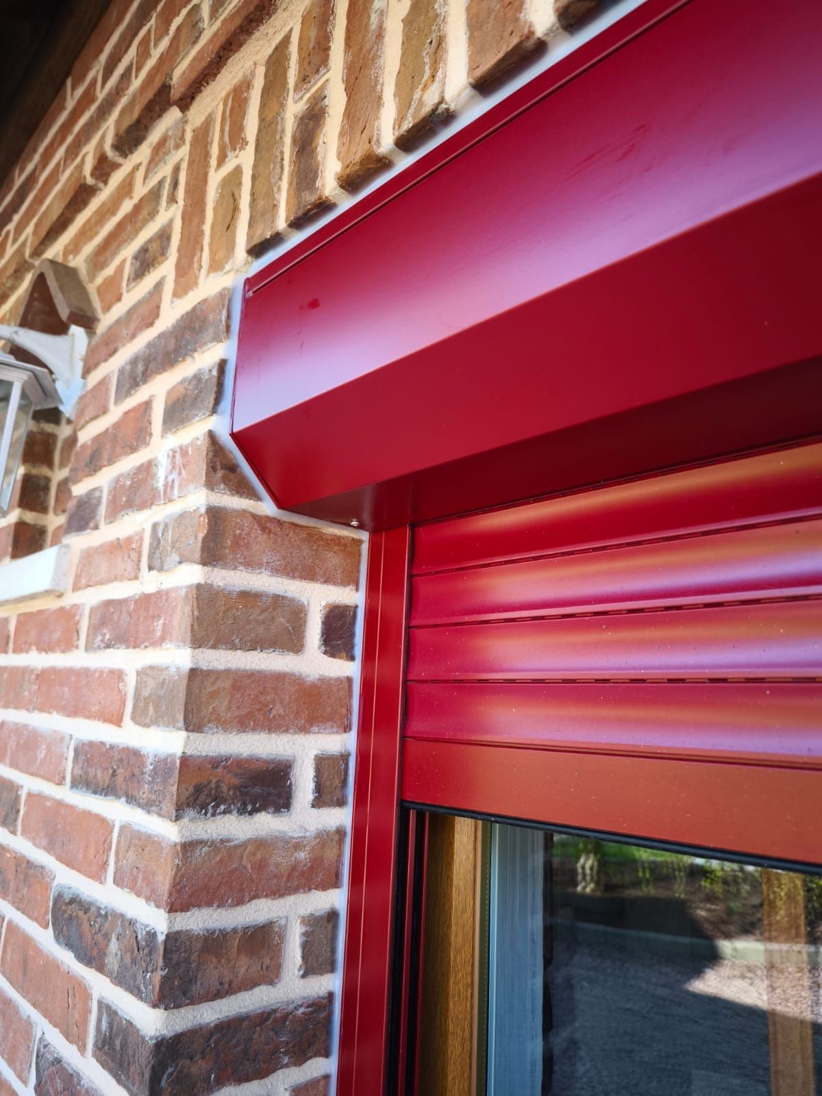 Un volet roulant rouge est sur un mur de briques à côté d'une fenêtre.
