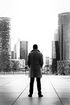 Un homme en trench-coat se tient devant l'horizon d'une ville.