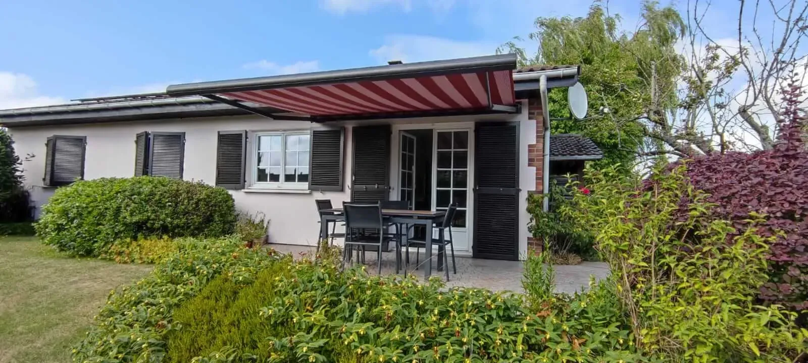 Une petite maison blanche avec un auvent rouge au-dessus du porche.