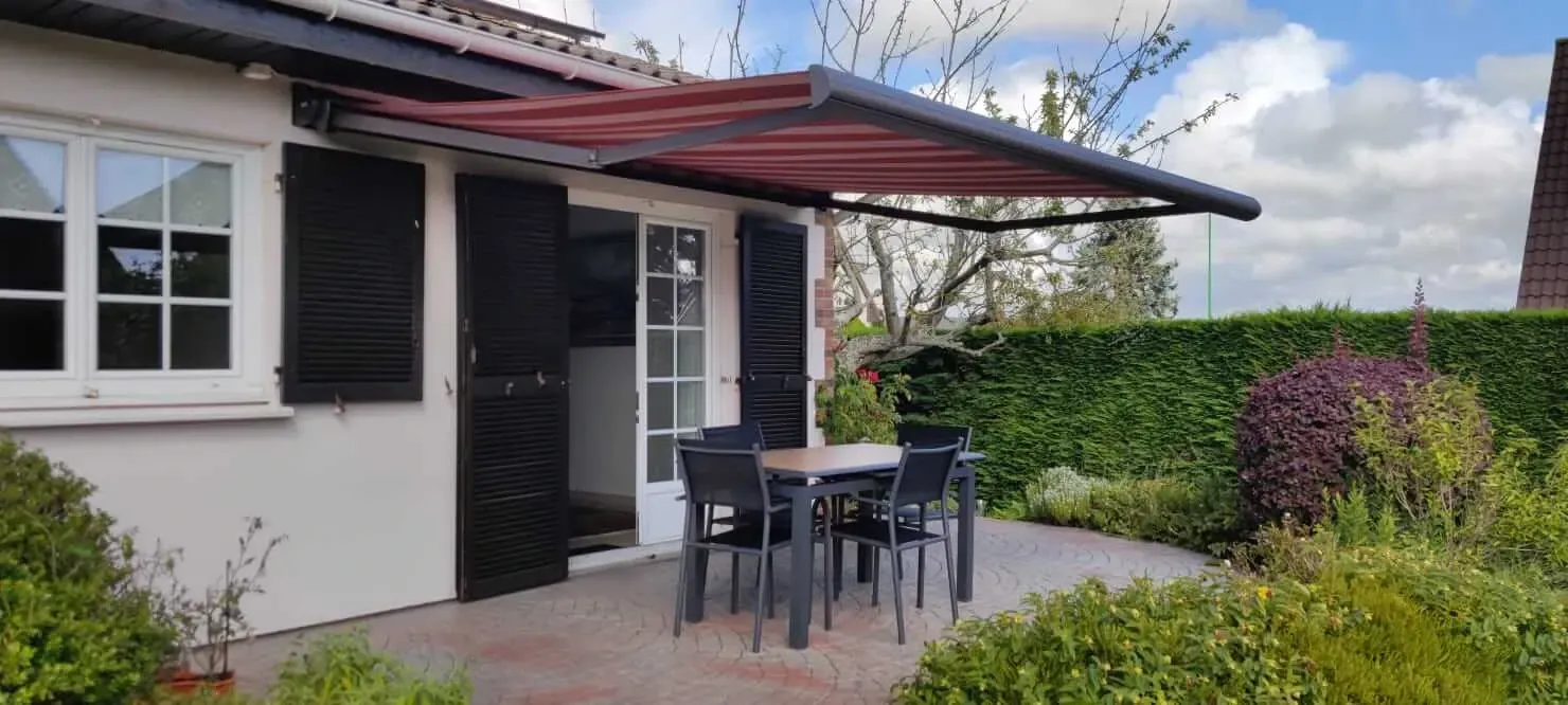 Une maison avec un patio avec une table et des chaises sous un store extérieur.
