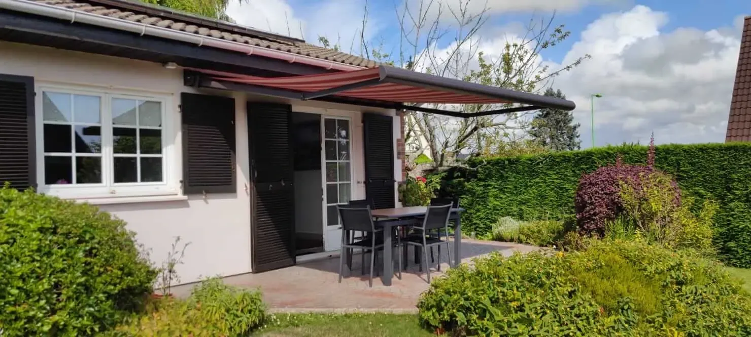 Une petite maison blanche avec des volets noirs et un patio avec une table et des chaises.