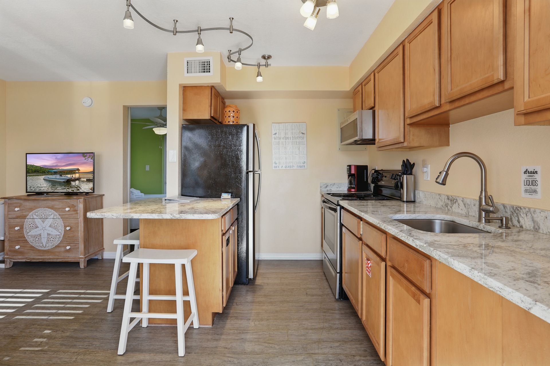 A kitchen with wooden cabinets , granite counter tops , stainless steel appliances and a flat screen tv.