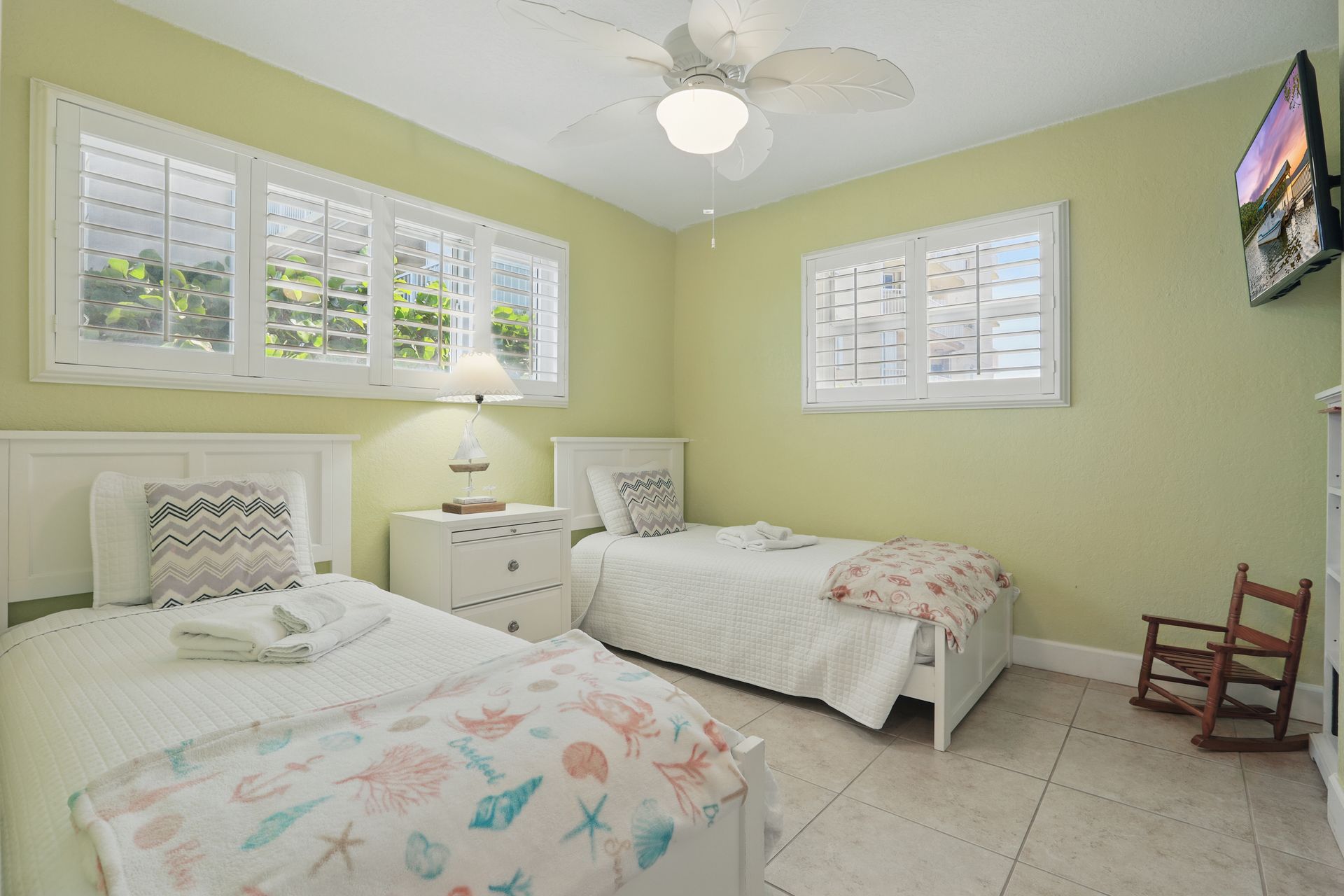 A bedroom with two beds , a television and a ceiling fan.