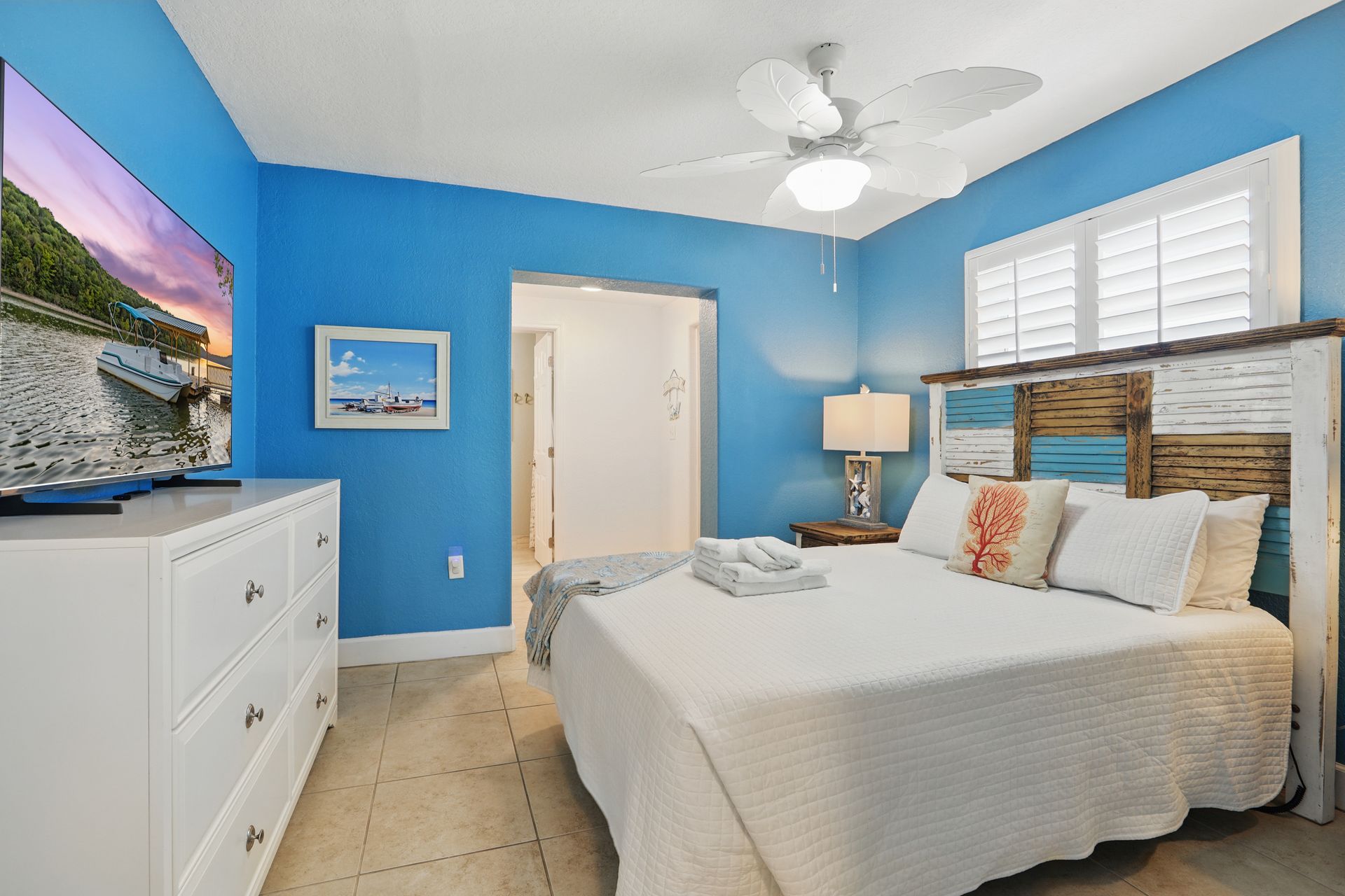 A bedroom with blue walls , a king size bed , a dresser , and a flat screen tv.