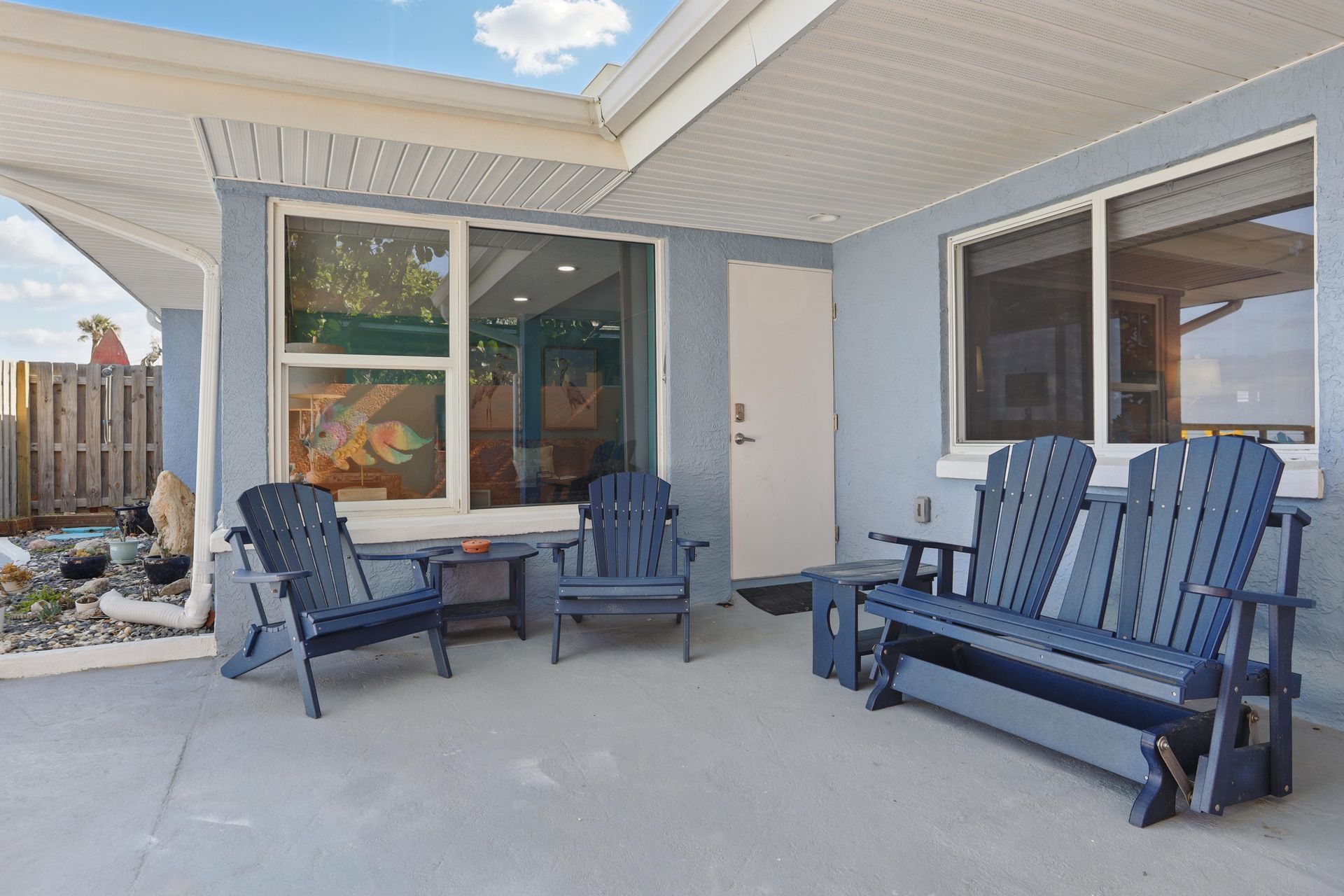 A patio with chairs , a table and a bench in front of a house.
