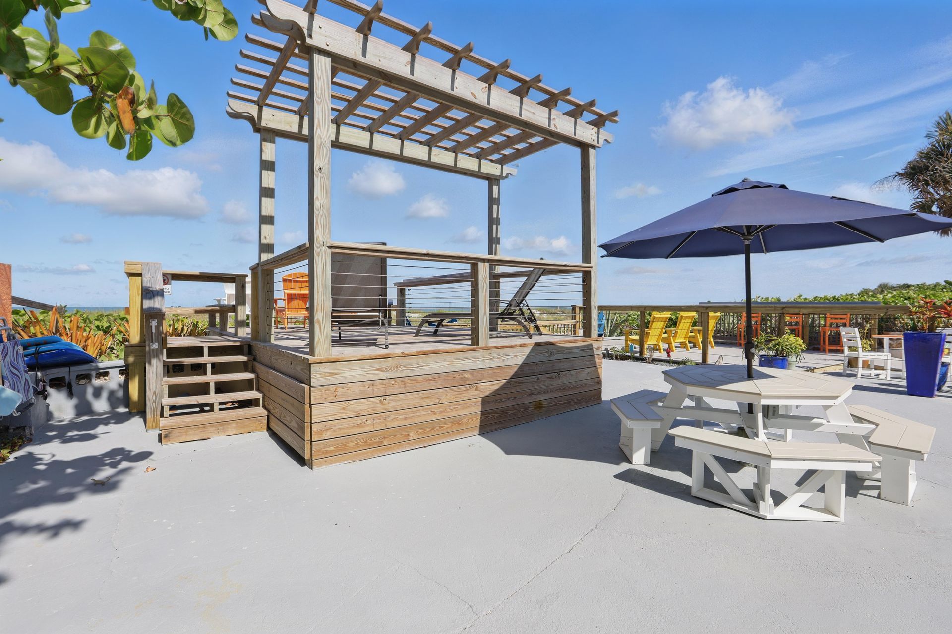 A wooden gazebo with umbrellas and picnic tables on a beach.