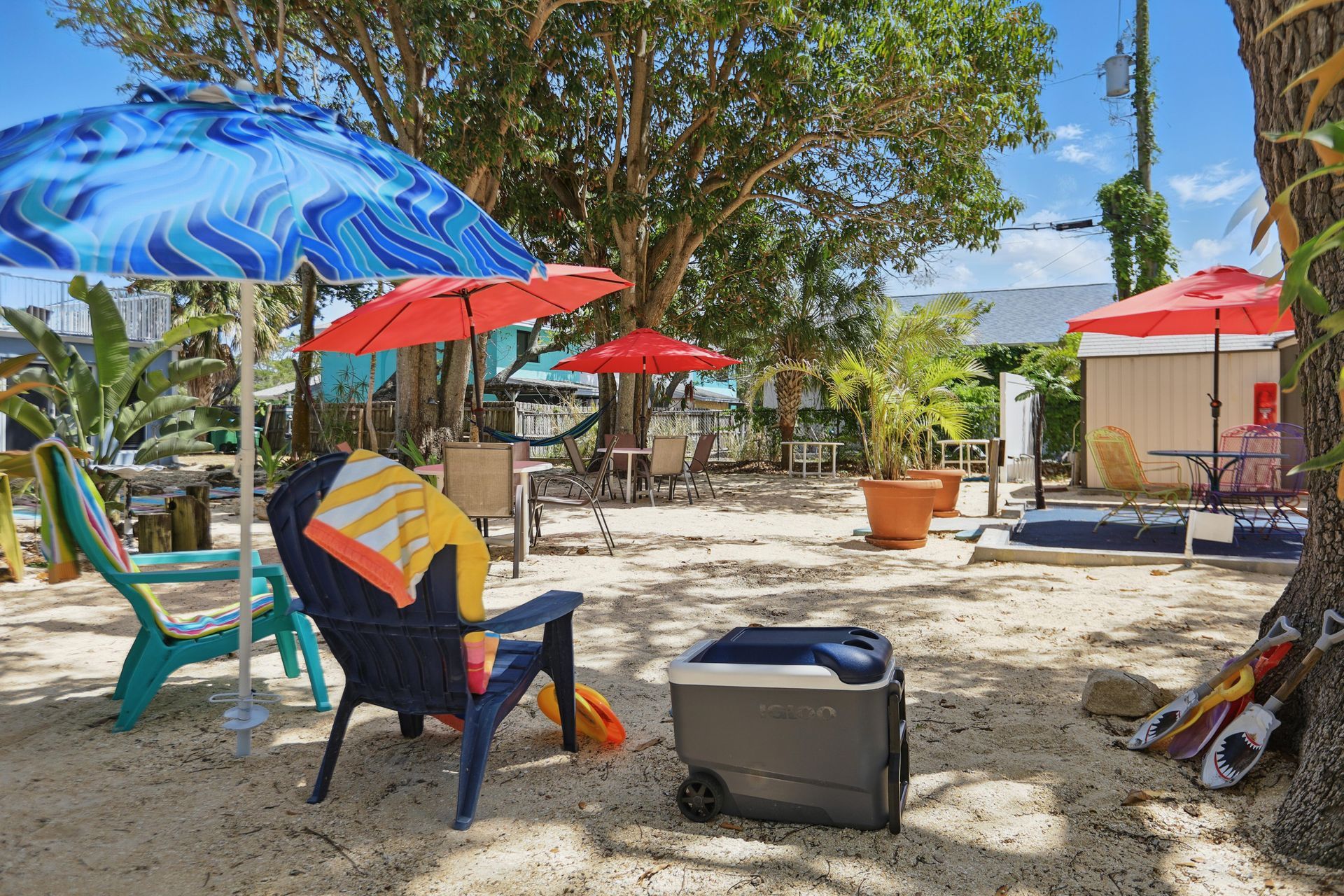 A patio with chairs , tables , umbrellas and a grill in front of a house.