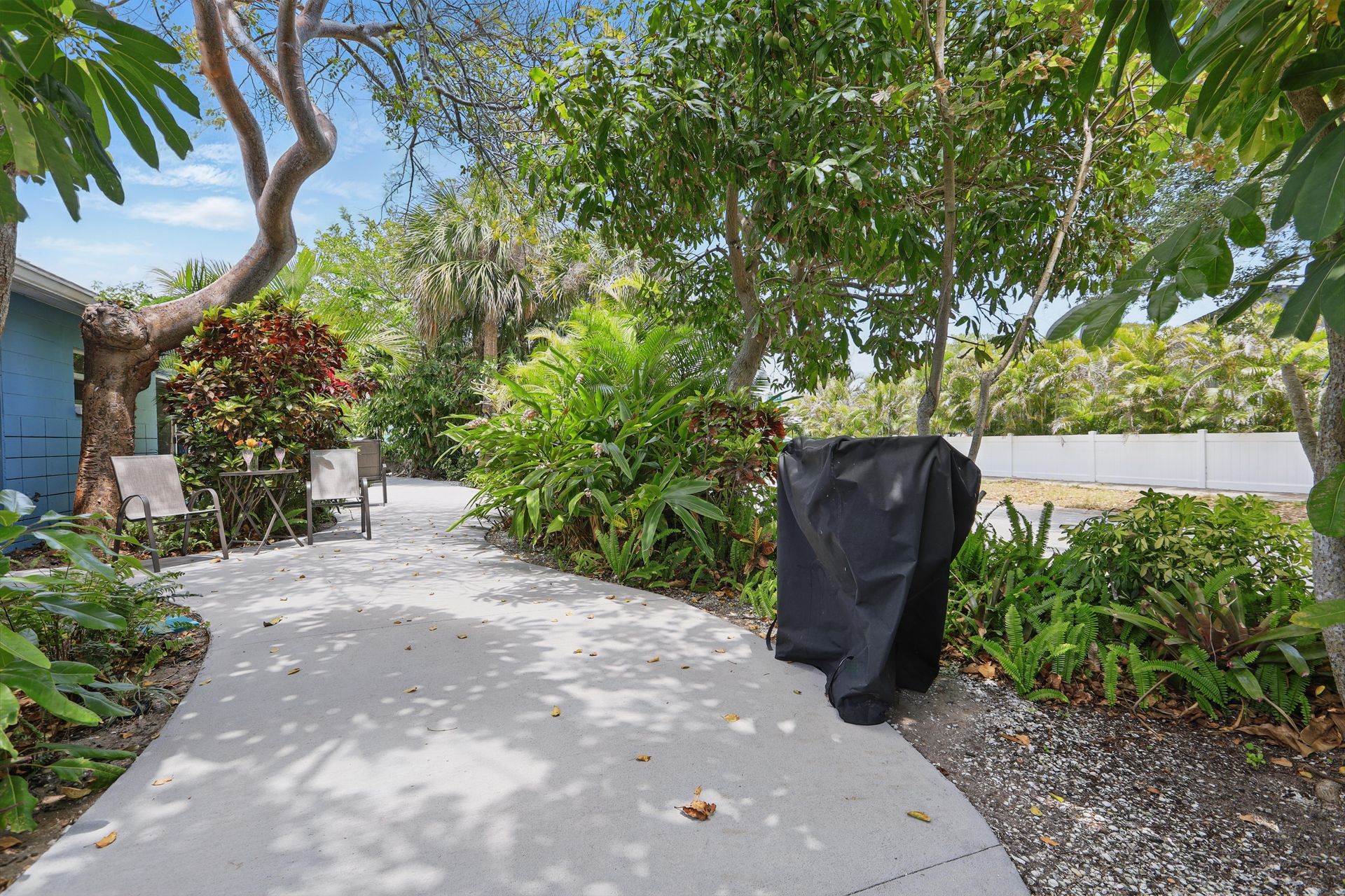 A bbq grill is sitting on a sidewalk next to a lush green garden.