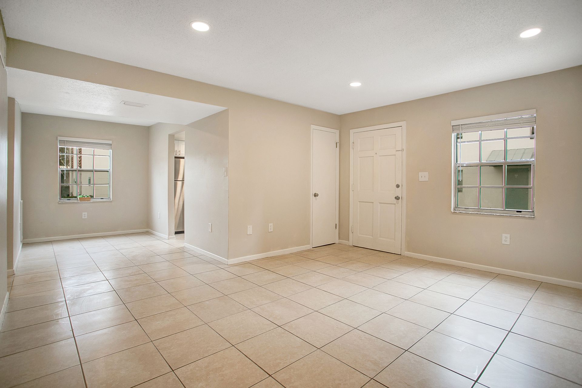 An empty living room with tile floors and two windows.