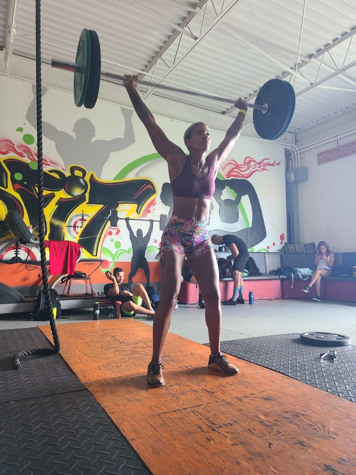 A woman is lifting a barbell over her head in a gym.
