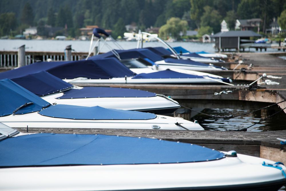 A row of boats with blue covers are docked at a dock.