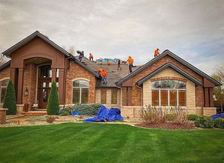 A group of people are working on the roof of a large brick house.