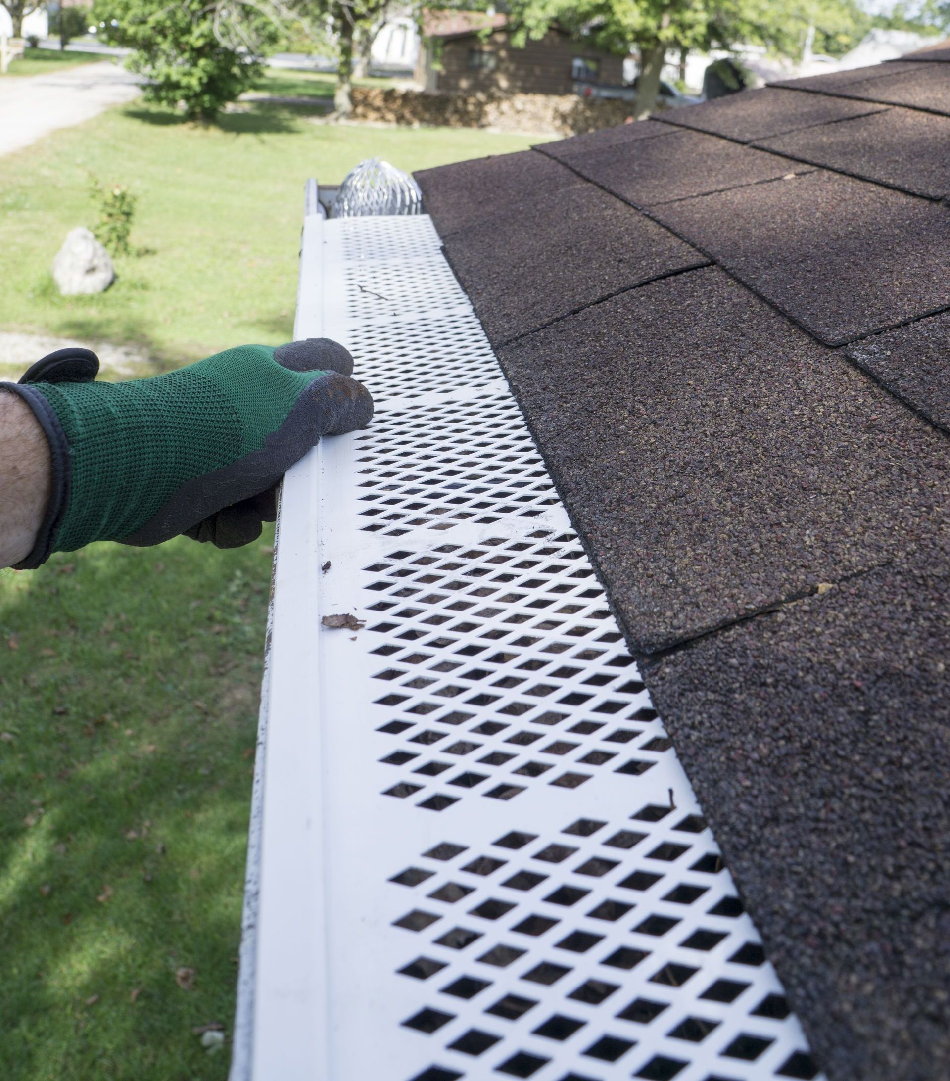 A person wearing green gloves is cleaning a gutter on a roof.