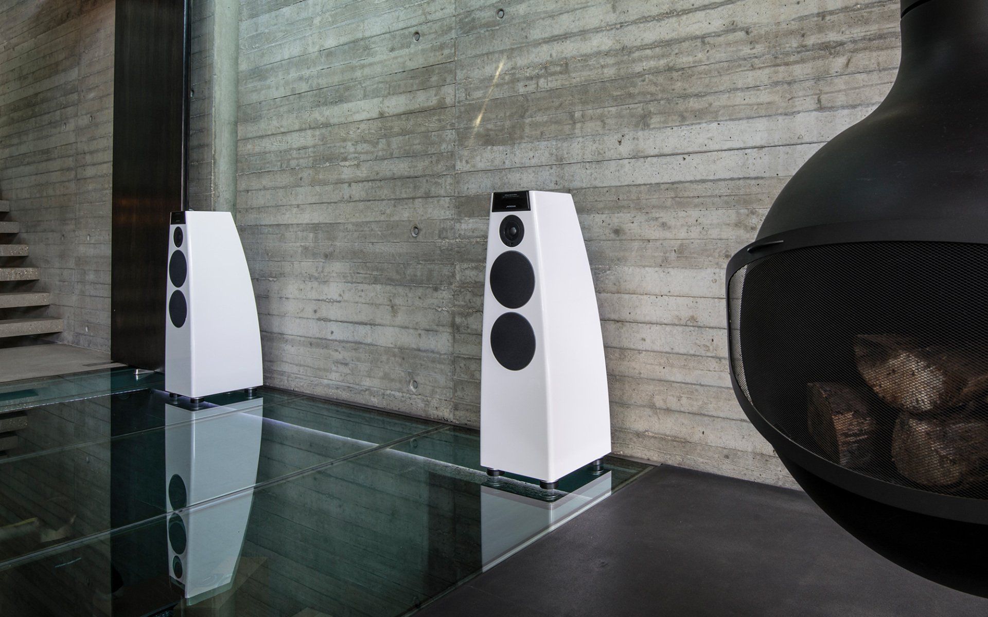 Two white speakers are sitting on a glass floor next to a fireplace.