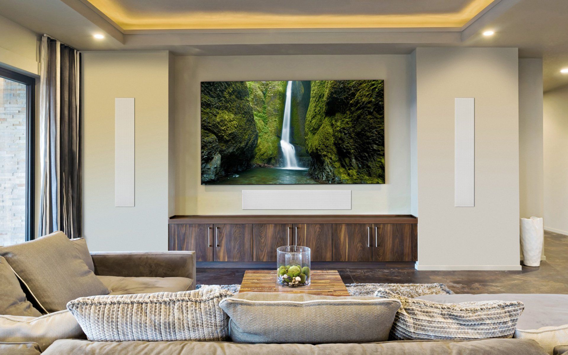 A living room with a couch , table , television and a picture of a waterfall on the wall.
