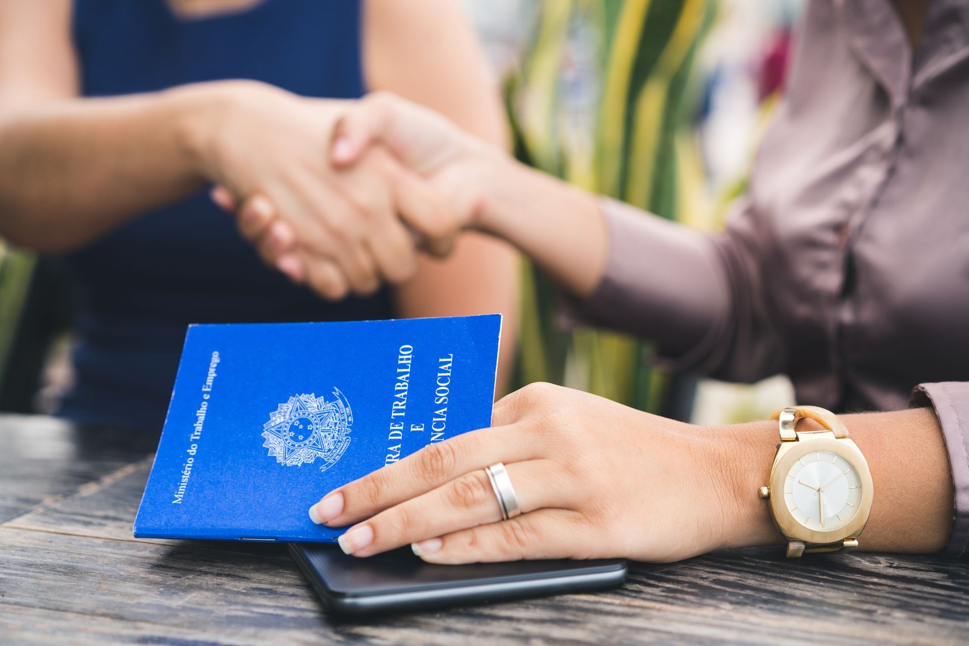 Two people shaking hands over a blue work document on a table. Two people shaking hands over a blue work document on a table.