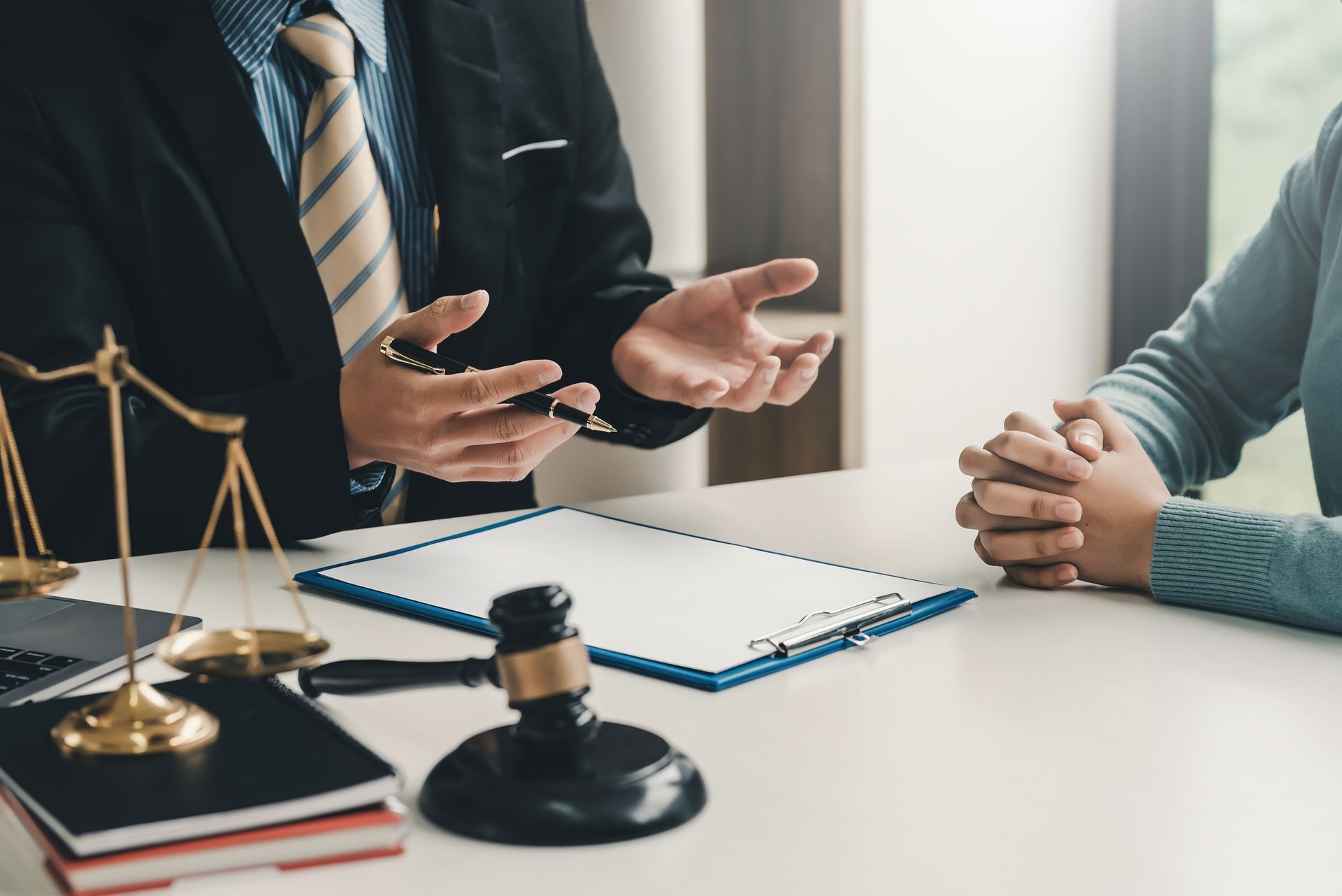 A Social Security attorney sitting in the office with a woman, on his desk with a gavel and a scale.