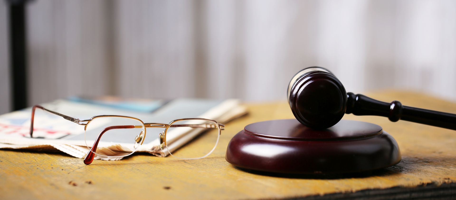 Glasses and gavel on wooden desk with papers in background.