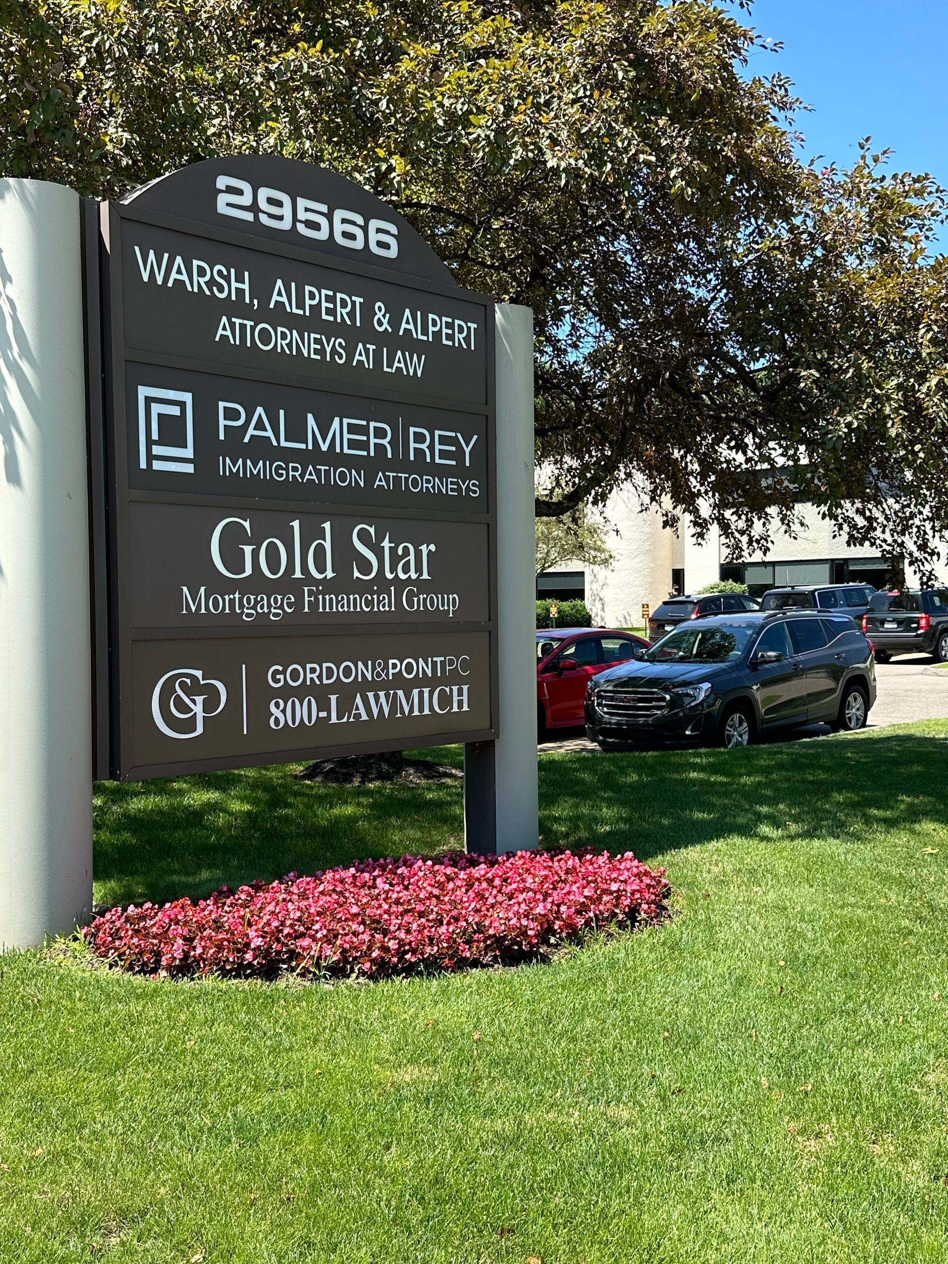 A sign for a business is sitting in the grass in front of a building.