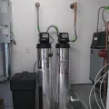 Two tall water softener tanks with gauges and pipes in a utility room