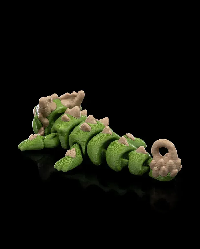A green and brown toy dragon is laying on its back on a black surface.