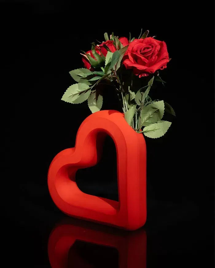 Two red roses in a red heart shaped vase on a black background.