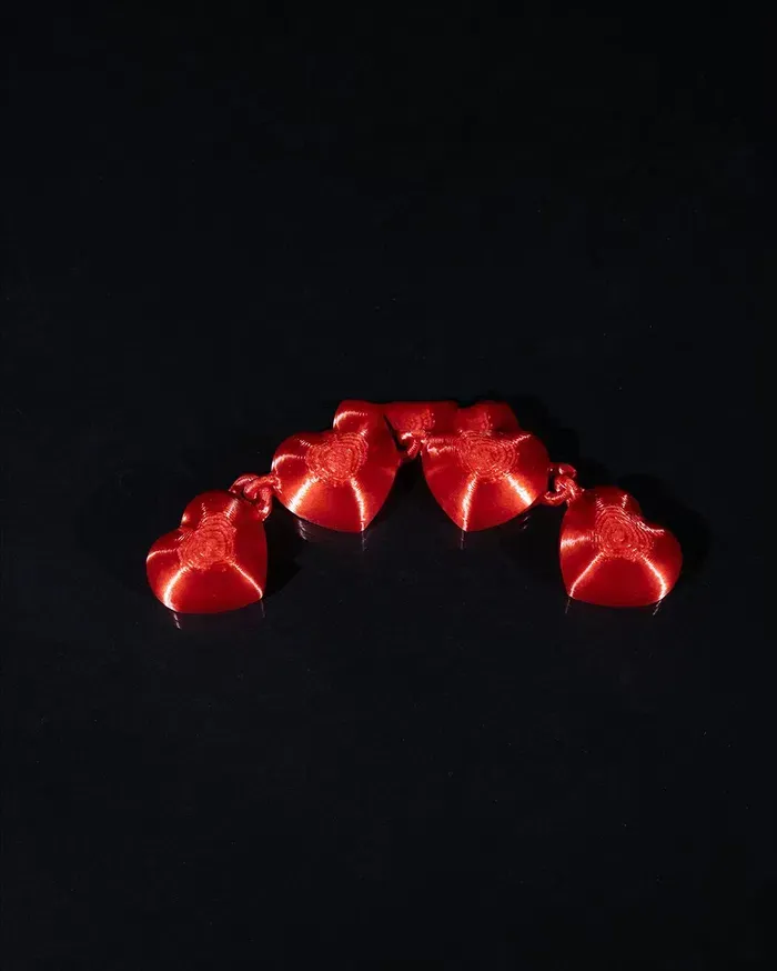 Two stuffed cats are holding a string of red hearts on a black surface.