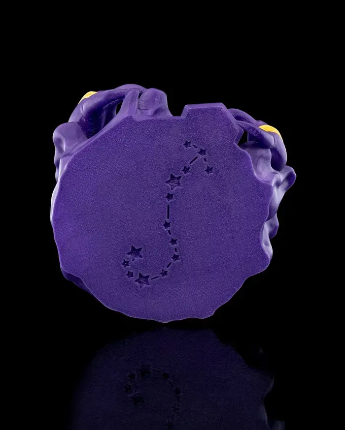 A purple scorpion figurine with a yellow tail is sitting on a black surface.