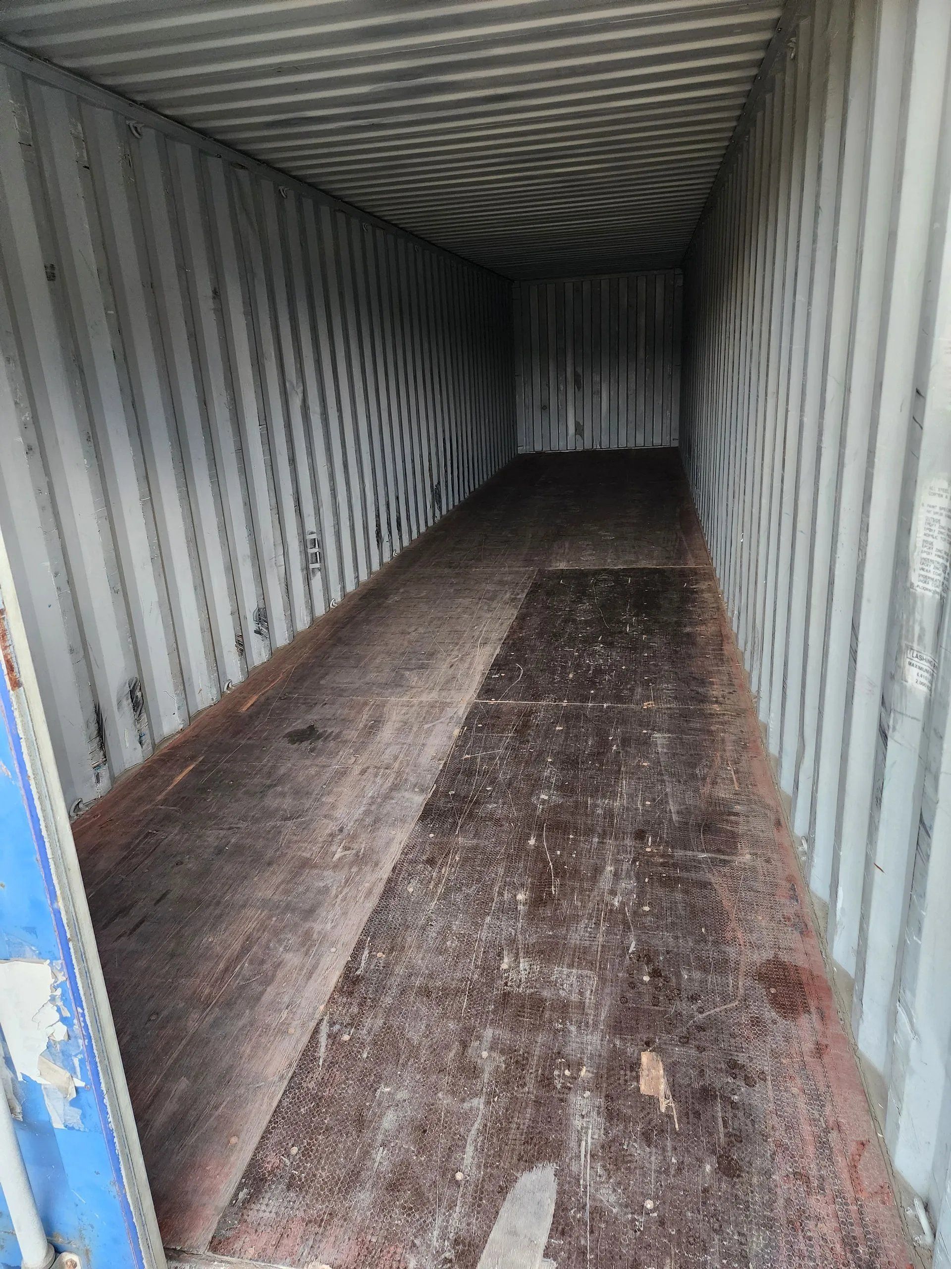 Inside of an empty cargo container with a rusty wooden floor and corrugated walls.