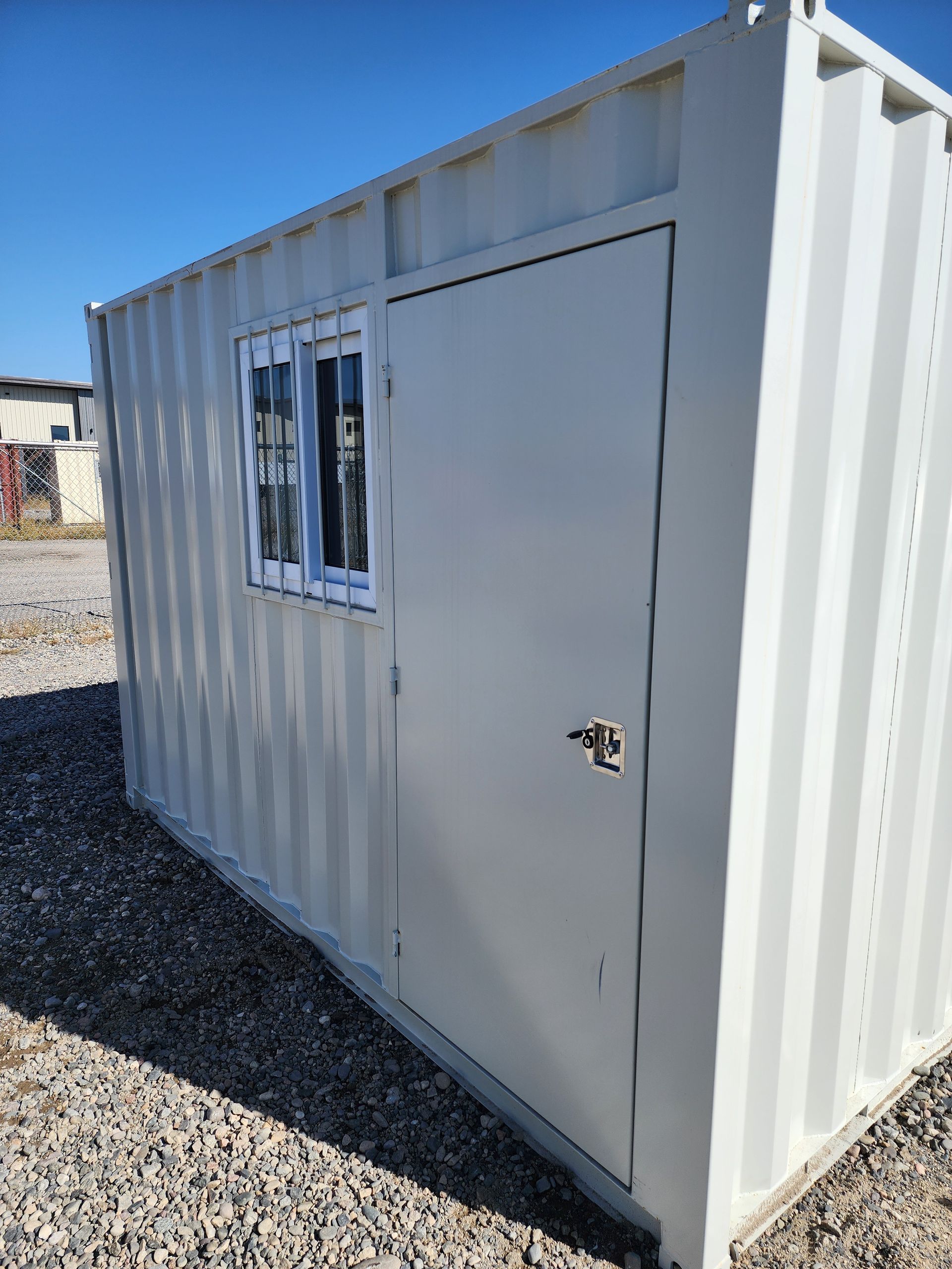 White shipping container with a door and small window under a blue sky.