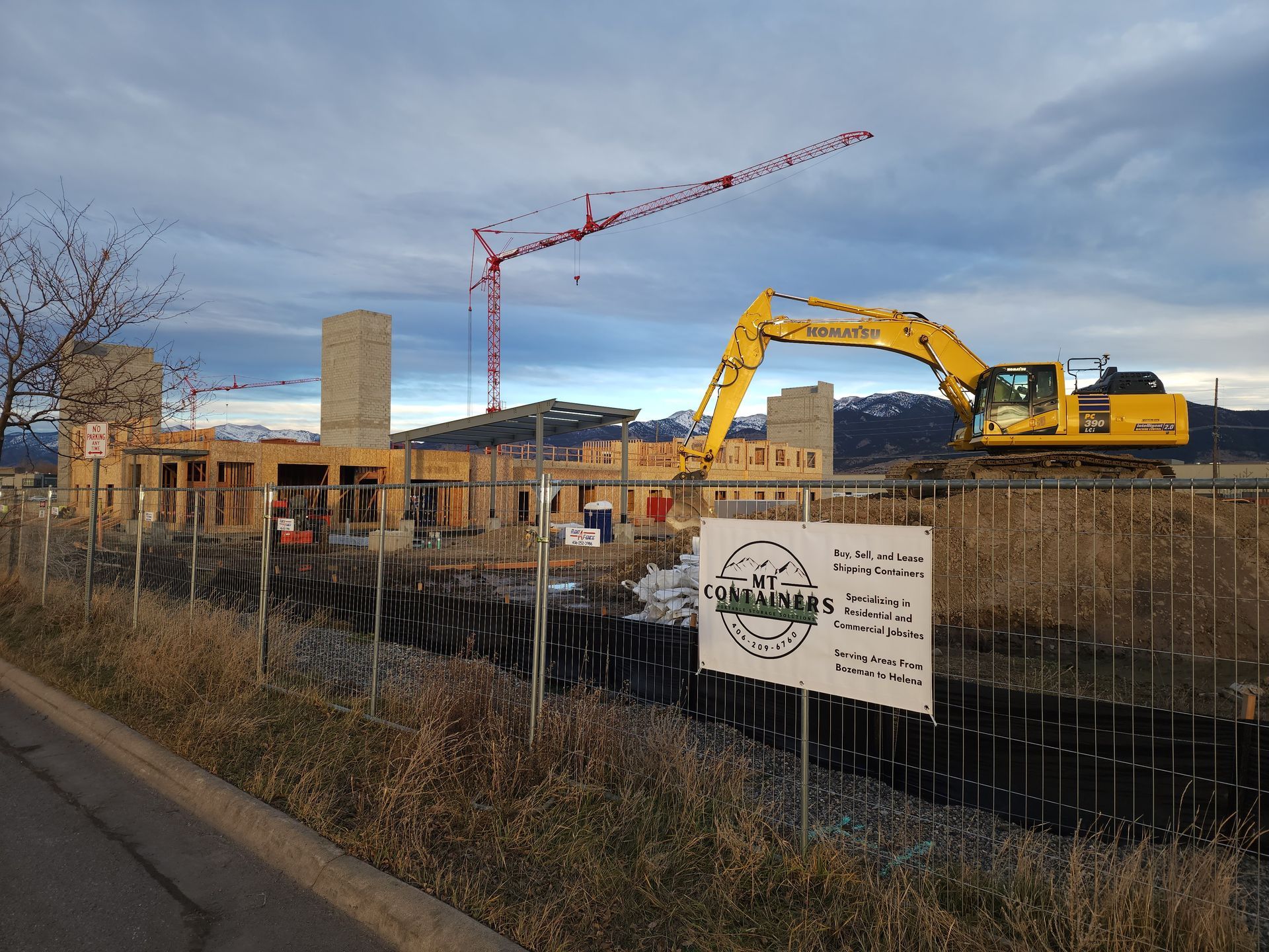 Construction site with crane and excavator; building under development with mountains in the background.