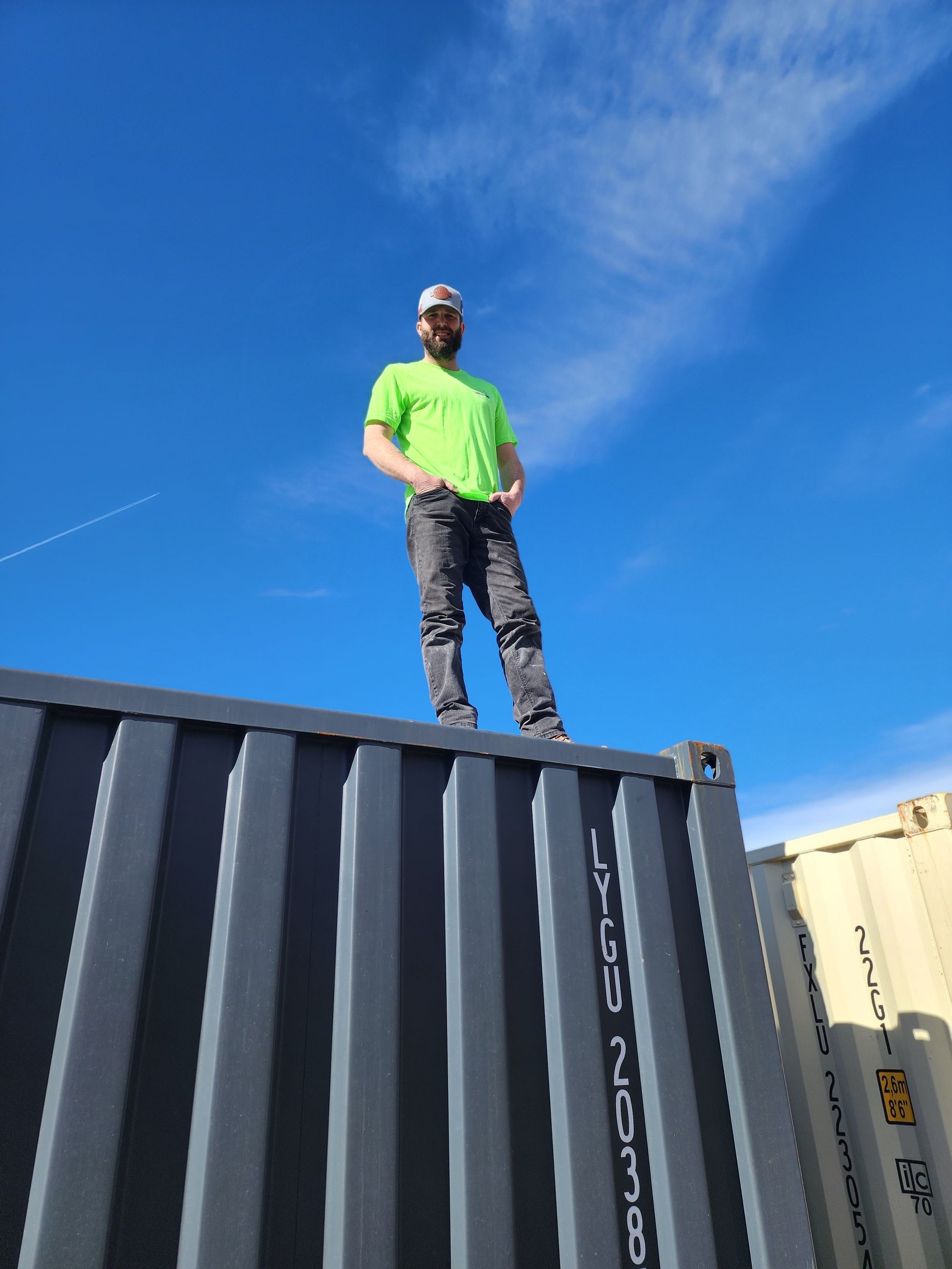Man standing on top of a shipping container, blue sky background.