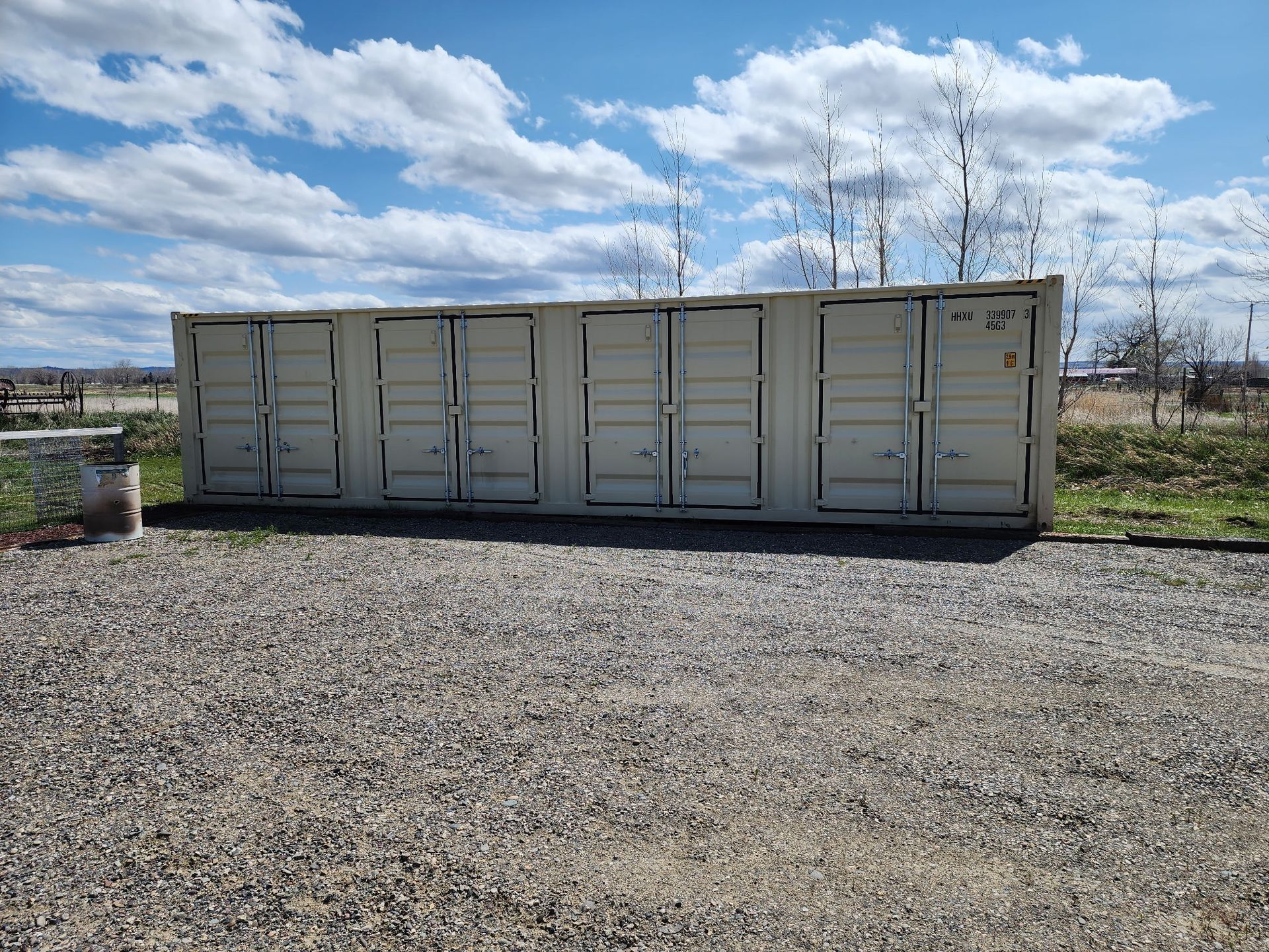 Storage containers with multiple doors on gravel under a cloudy sky.