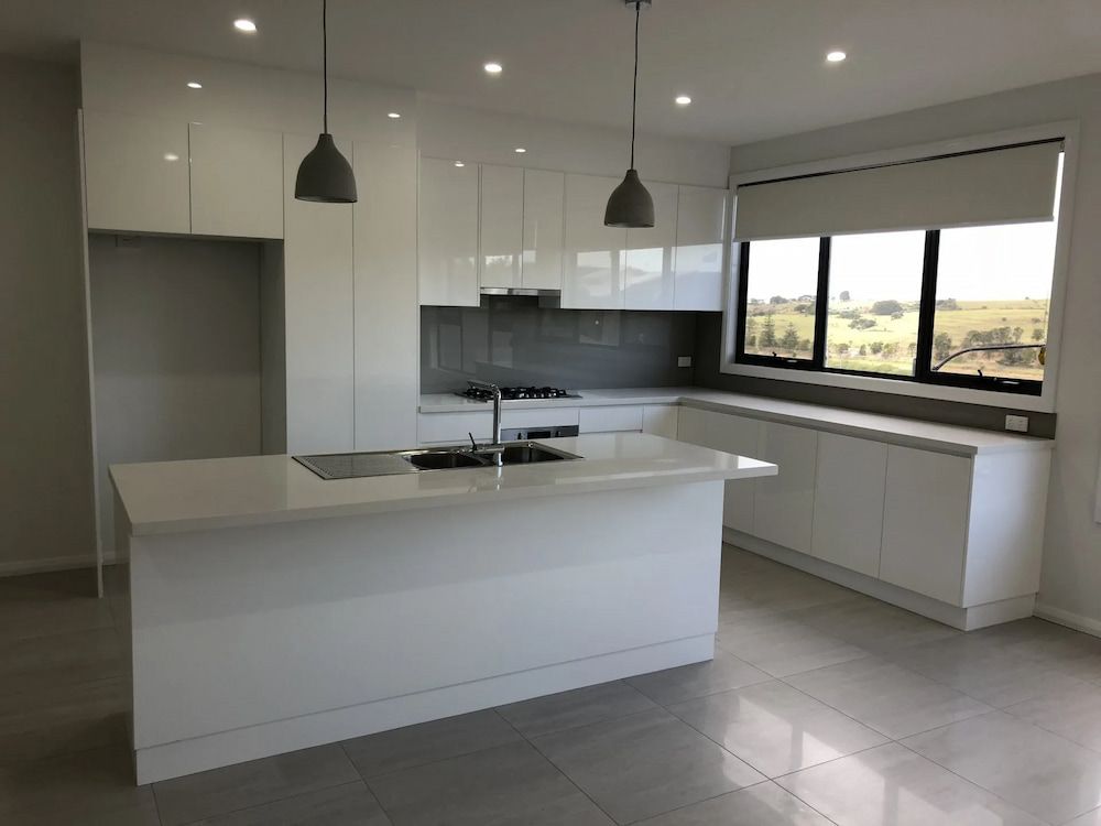 An Empty Kitchen With White Cabinets And A Large Island — United Kitchens and Joinery in Oak Flats, NSW
